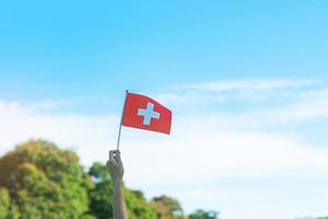 mano que sostiene la bandera suiza sobre fondo de cielo azul. día nacional de suiza y conceptos de celebración feliz foto