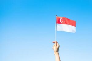 mano sosteniendo la bandera de singapur sobre fondo de cielo azul. día nacional de singapur y conceptos de celebración feliz foto