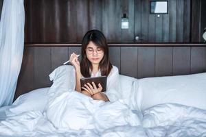 Happy woman using tablet for social media, young female watching movies on computer pad on bed at home. technology, network, online shopping, e commerce, lifestyle and digital communication concept photo