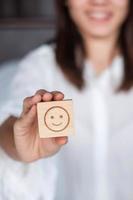 Happy Woman holding smile emotion face block. Customer choose Emoticon for user reviews. Service rating, mental health, positive thinking, satisfaction, evaluation and feedback concept photo