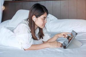 Happy woman using tablet for social media, young female watching movies on computer pad on bed at home. technology, network, online shopping, e commerce, lifestyle and digital communication concept photo