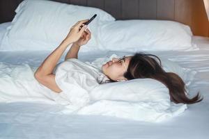 woman using smartphone for social media, young female watching movies by mobile phone on bed at home. technology, network, online shopping, e commerce, lifestyle and digital communication concept photo