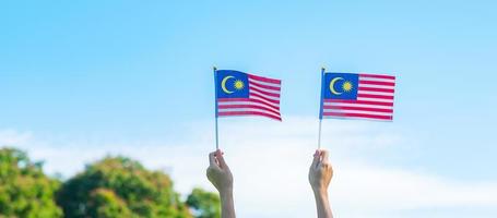 mano que sostiene la bandera de malasia sobre fondo de cielo azul. septiembre día nacional de malasia y agosto día de la independencia foto