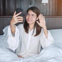 Happy woman using smart phone for video call, female meeting  online by mobile phone on bed. technology, network, work from home, lifestyle and digital communication concept photo