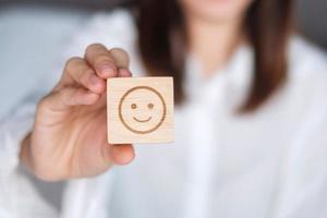 mujer feliz sosteniendo un bloque de cara de emoción de sonrisa. el cliente elige el emoticono para las reseñas de los usuarios. calificación de servicio, salud mental, pensamiento positivo, satisfacción, evaluación y concepto de retroalimentación foto