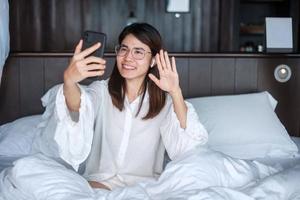 Happy woman using smart phone for video call, female meeting  online by mobile phone on bed. technology, network, work from home, lifestyle and digital communication concept photo