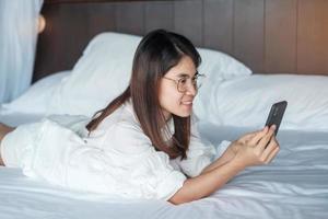 woman using smartphone for social media, young female watching movies by mobile phone on bed at home. technology, network, online shopping, e commerce, lifestyle and digital communication concept photo