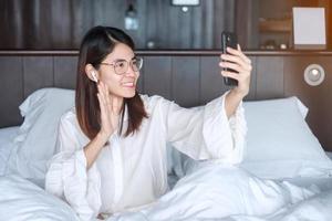 Happy woman using smart phone for video call, female meeting  online by mobile phone on bed. technology, network, work from home, lifestyle and digital communication concept photo