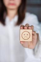 Woman holding angry emotion face block. Customer choose Emoticon for user reviews. Service rating, mental health, positive thinking, satisfaction, evaluation and feedback concept photo