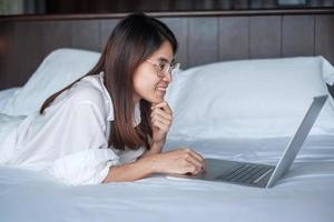 Happy woman using laptop for work, female meeting  online by computer notebook on bed. technology, network, work from home, lifestyle and digital communication concept photo