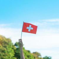 mano que sostiene la bandera suiza sobre fondo de cielo azul. día nacional de suiza y conceptos de celebración feliz foto