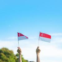 mano sosteniendo la bandera de singapur sobre fondo de cielo azul. día nacional de singapur y conceptos de celebración feliz foto
