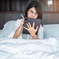 Happy woman using tablet for video call, female meeting  online by computer pad on bed. technology, network, work from home, lifestyle and digital communication concept photo