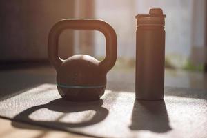 gym equipment, kettlebell dumbbell weight and bottle of water on yoga mat at home. photo