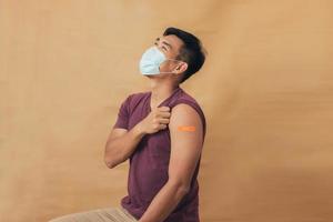 Asian man showing shoulders after getting a vaccine. Happy man showing arm with band-aids on after vaccine injection. photo