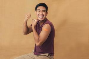 Asian man showing shoulders after getting a vaccine. Happy man showing arm with band-aids on after vaccine injection. photo