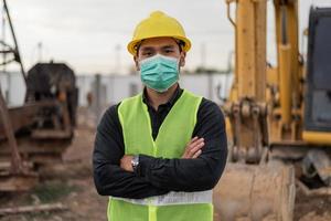 engineer man wearing face mask and working in building site. Asian worker man standing and crossed arms in construction site. photo