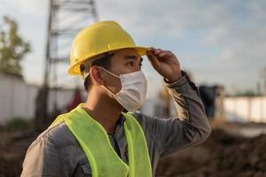 Engineer man wearing face mask and working in building site. Young worker man working in construction site. photo