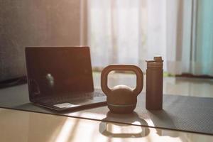 gym equipment, kettlebell dumbbell weight and laptop on yoga mat at home.