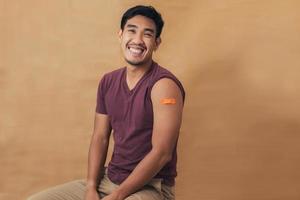 Asian man showing shoulders after getting a vaccine. Happy man showing arm with band-aids on after vaccine injection. photo