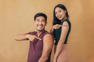 Asian man and woman showing shoulders after getting a vaccine. Happy couple showing arm with band-aids on after vaccine injection. photo