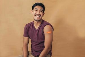 Asian man showing shoulders after getting a vaccine. Happy man showing arm with band-aids on after vaccine injection. photo