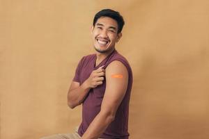 Asian man showing shoulders after getting a vaccine. Happy man showing arm with band-aids on after vaccine injection. photo