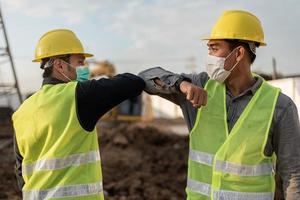 Engineers man wearing face mask and touching with elbow in building site. Construction manager and engineer man wearing face mask have a greeting by touching the elbow photo