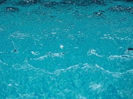 Rain drops falling blue water in pool background ripples on the surface texture, glittering bokeh abstract photo