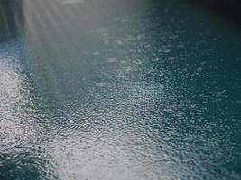 Rain drops falling blue water in pool background ripples on the surface texture, glittering bokeh abstract photo