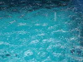 Rain drops falling blue water in pool background ripples on the surface texture, glittering bokeh abstract photo