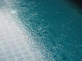 gotas de lluvia que caen agua azul en el fondo de la piscina ondulaciones en la textura de la superficie, resumen de bokeh brillante foto