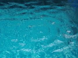 Rain drops falling blue water in pool background ripples on the surface texture, glittering bokeh abstract photo