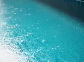 Rain drops falling blue water in pool background ripples on the surface texture, glittering bokeh abstract photo