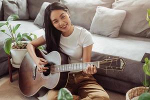 Woman playing guitar at home. Beautiful woman smiling and playing guitar with her plants in living room. photo