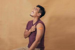 Asian man showing shoulders after getting a vaccine. Happy man showing arm with band-aids on after vaccine injection. photo