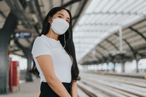 mujer asiática con máscara protectora de pie y esperando el tren del cielo. mujer con máscara protectora quirúrgica en un transporte público. nuevo concepto normal. foto