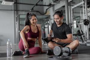 ejercicio de mujer asiática con entrenador personal en el gimnasio. entrenador personal que muestra y habla sobre el plan de ejercicio con una mujer sana. foto