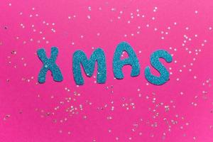 Word Xmas on pink background with glittered little stars. Christmas inscription with space for text writing, greeting. Concept banner for Christmas card, advertising. Top view. High quality photo