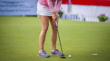 golfista empujando la pelota de golf blanca al hoyo en el campo de golf en el juego de competencia de golf, rayos de luz solar y fondo borroso foto