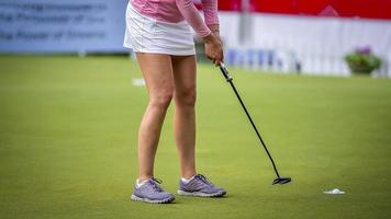 golfista empujando la pelota de golf blanca al hoyo en el campo de golf en el juego de competencia de golf, rayos de luz solar y fondo borroso foto