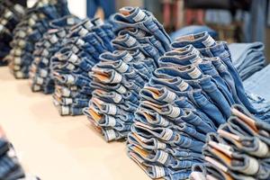 Denim jeans stack on wood table in clothing store, shopping photo