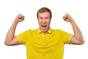 Funny young man in casual yellow T-shirt raising hands and rejoicing of success, isolated background photo