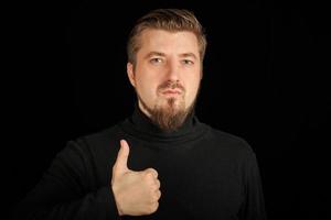 Serious bearded man with thumbs up gesture, black background photo