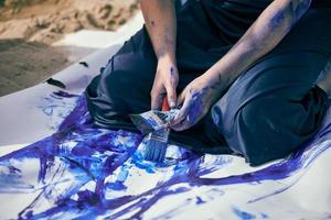 Female performance artist in dark blue dress smeared with blue gouache painting with wide strokes on canvas photo