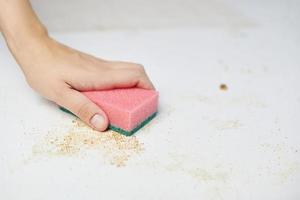 Cleaning kitchen table. Pink sponge in woman hand removes dirt, bread crumbs and leftovers. Household chores photo