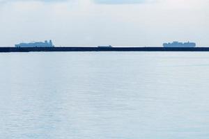 Seascape with cargo ships on horizon. Coastline in bay. Ships carry freight containers, fishing and park. photo