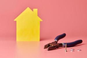 concepto de renovación de la casa. reparar y redecorar el hogar. alicates de liniero, tornillos y figura en forma de casa amarilla sobre fondo rosa. foto