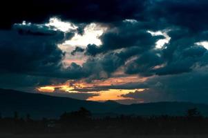 la puesta de sol es un montón de nubes negras, la luz naranja brillante brilla desde el grupo de nubes de lluvia, montaña de silueta foto