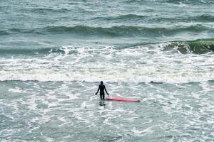 Male surfer in swimsuit in sea with red surfboard photo